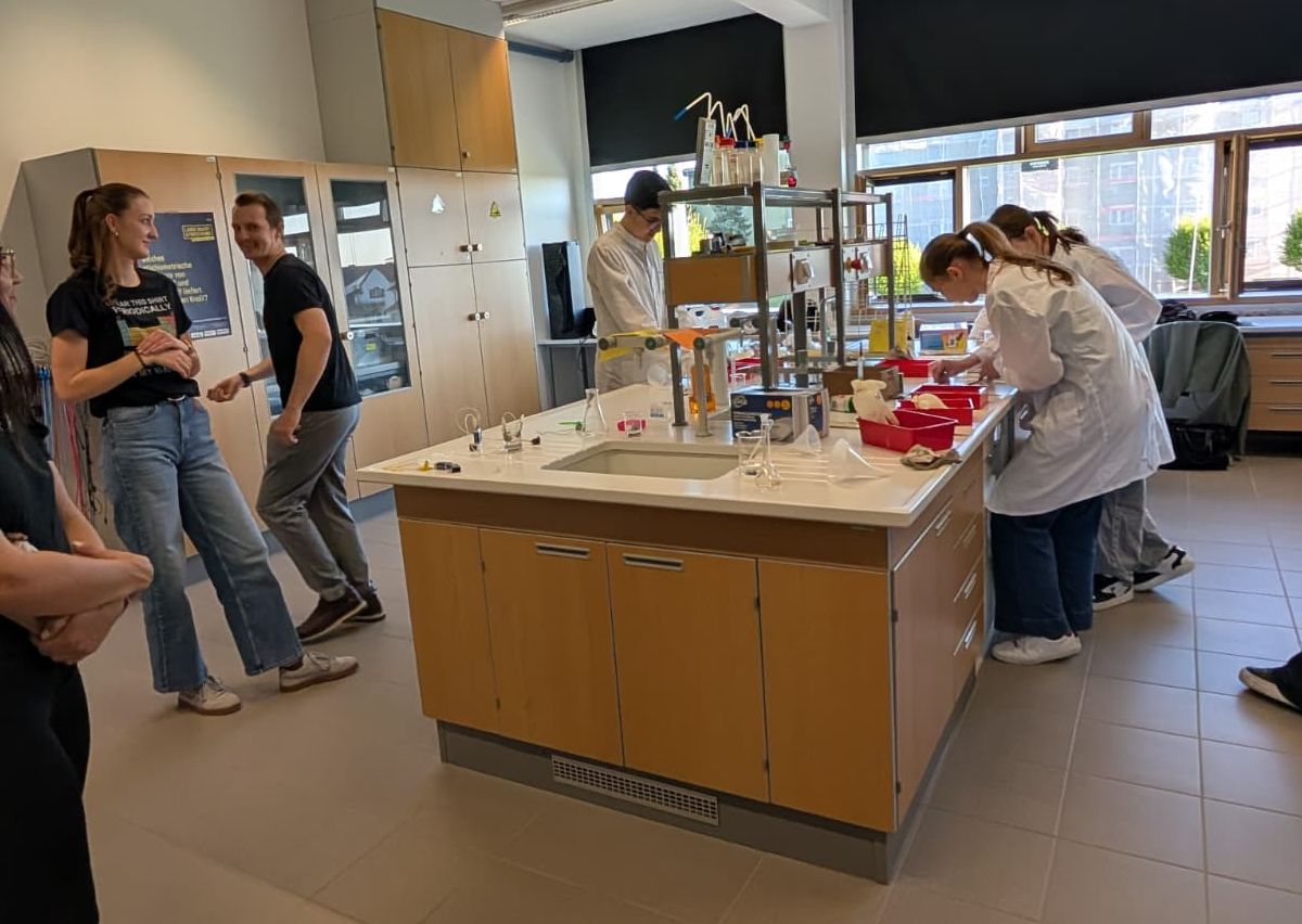 Chemielabor mit Labortisch, Glasgeräten und Schülerinnen in Laborkitteln