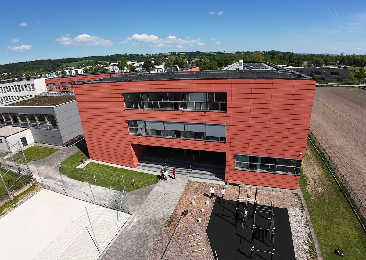 Drohnenfoto: rote Fassade und Haupteingang der HTL Perg, davor der Workoutpark