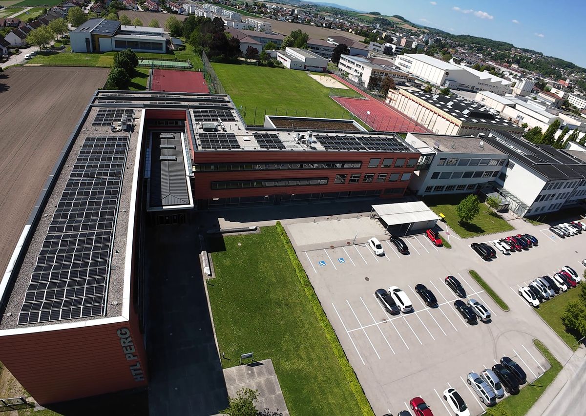 Drohnenfoto: Photovoltaikanlage auf dem Schuldach, daneben Parkplatz und Sportanlage