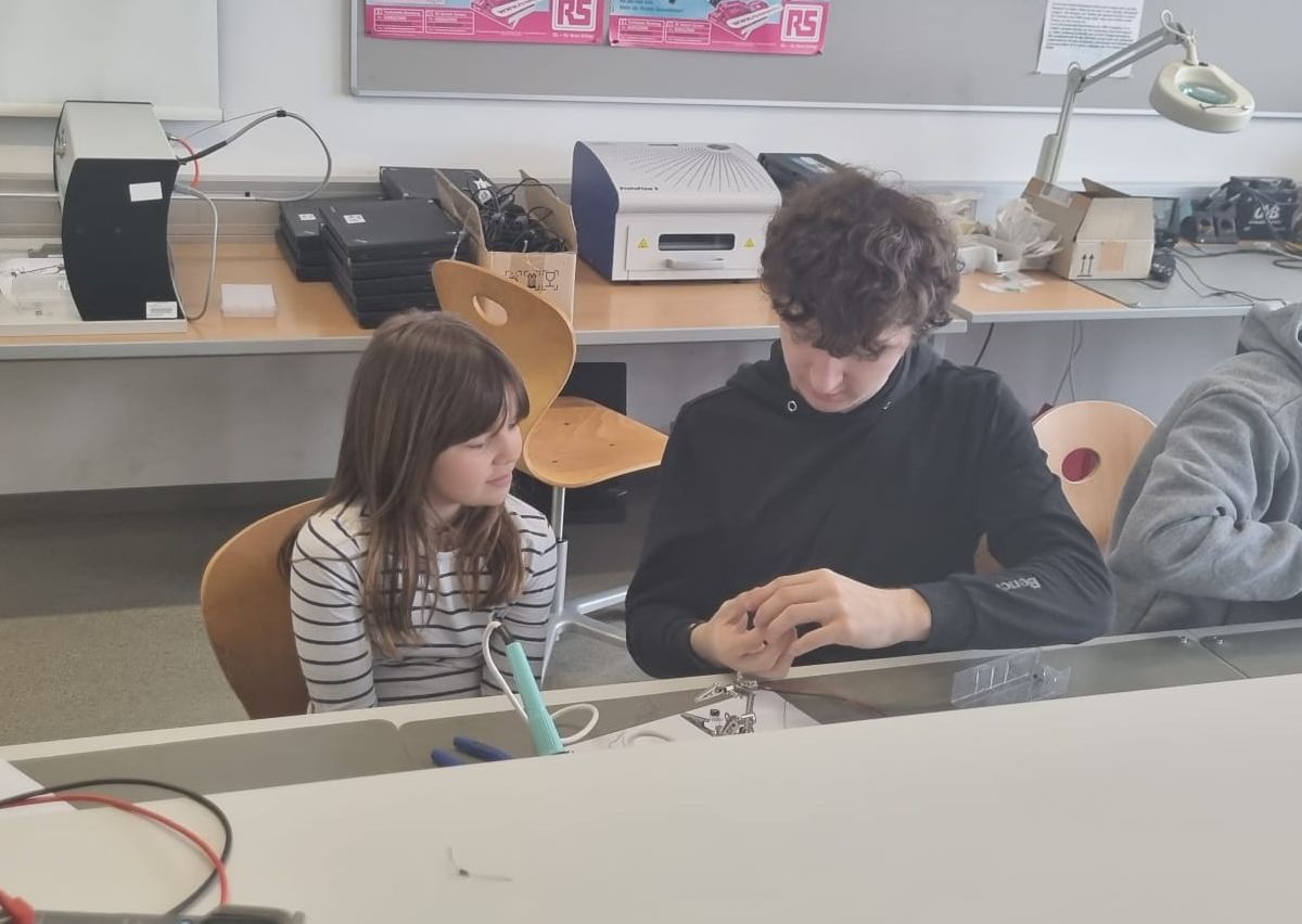 Mädchen und HTL-Schüler bauen an einer Elektronikschaltung am Laborarbeitsplatz